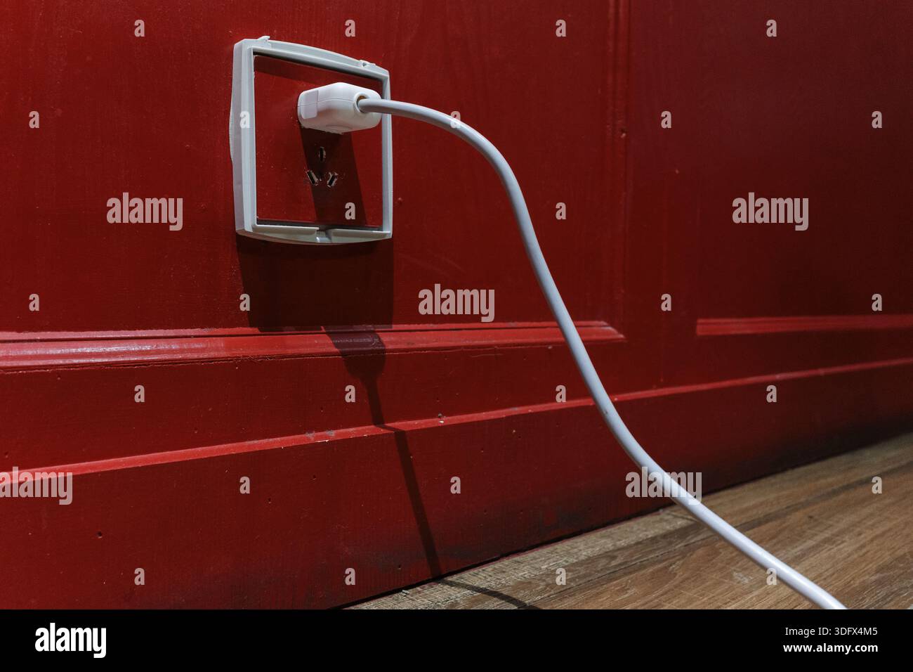 A white power cord plugs into a socket against a deep red wall. Bold color contrast and clean lines make for versatile commercial imagery. Stock Photo