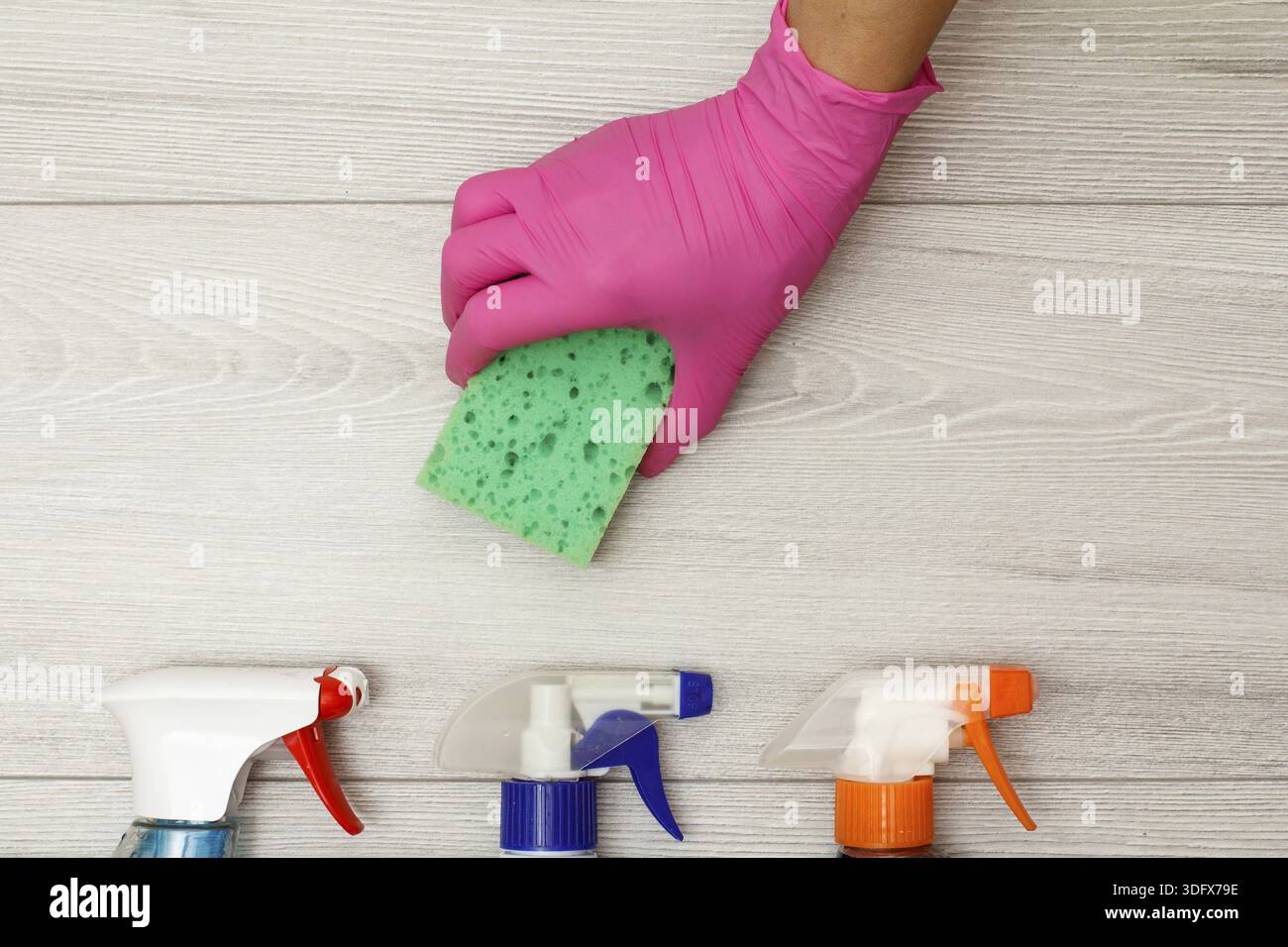 Hand in pink rubber glove holding sponge with bottles of detergent on ...