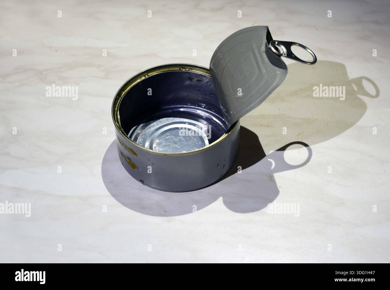 open and empty rounded can on a table with its  shadow on a table surface Stock Photo