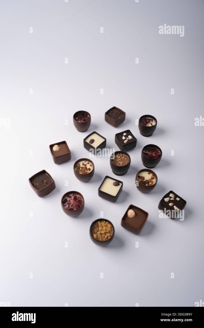 artisanal assorted chocolate bonbons and truffles arranged on a soft white backdrop, minimalist studio with neutral lighting, creamy fillings, nut and Stock Photo