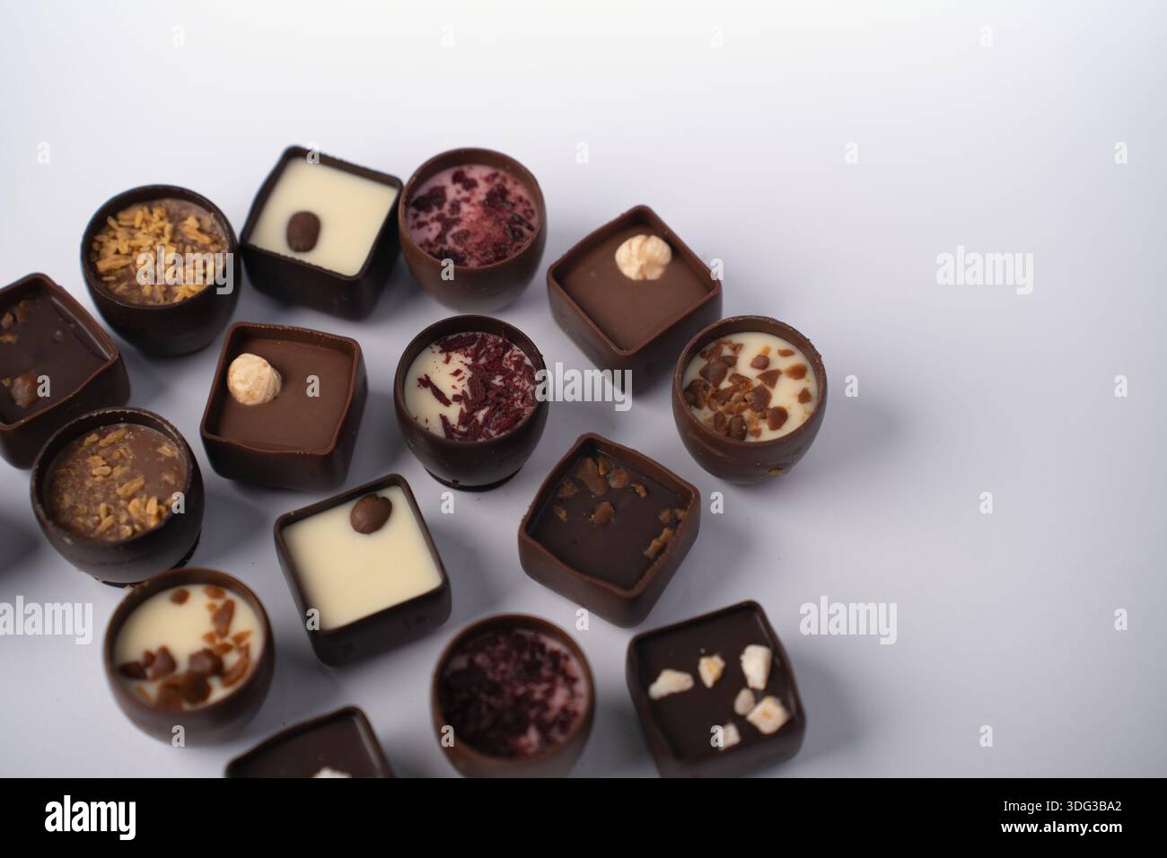 assorted artisanal chocolate bonbons arranged on a soft pale surface, featuring round and square shells filled with creamy ganache, white and dark cen Stock Photo