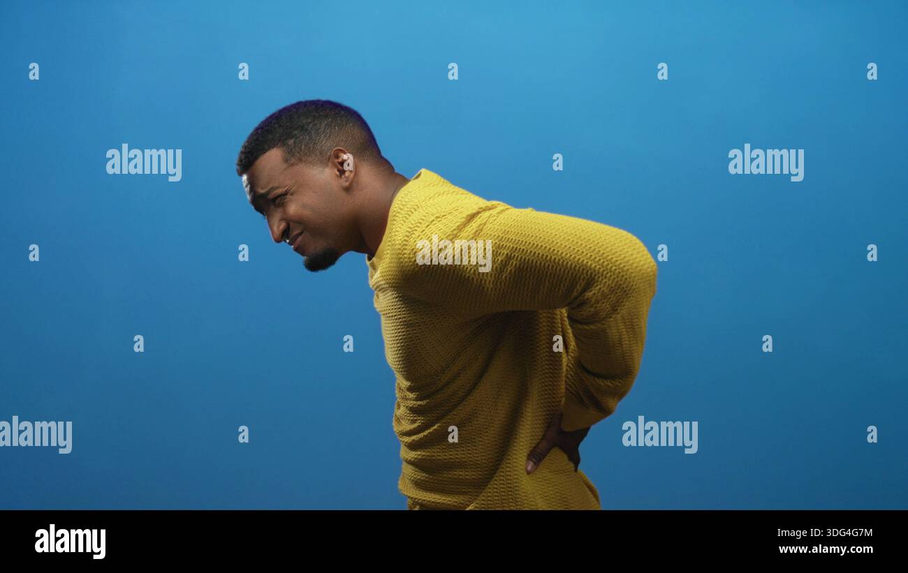 Hackache Young black man clutching abdomen with one hand and pressing lower back ...