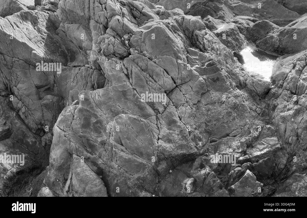 Monochrome photograph of rugged coastal rocks with sharp cracks and ...