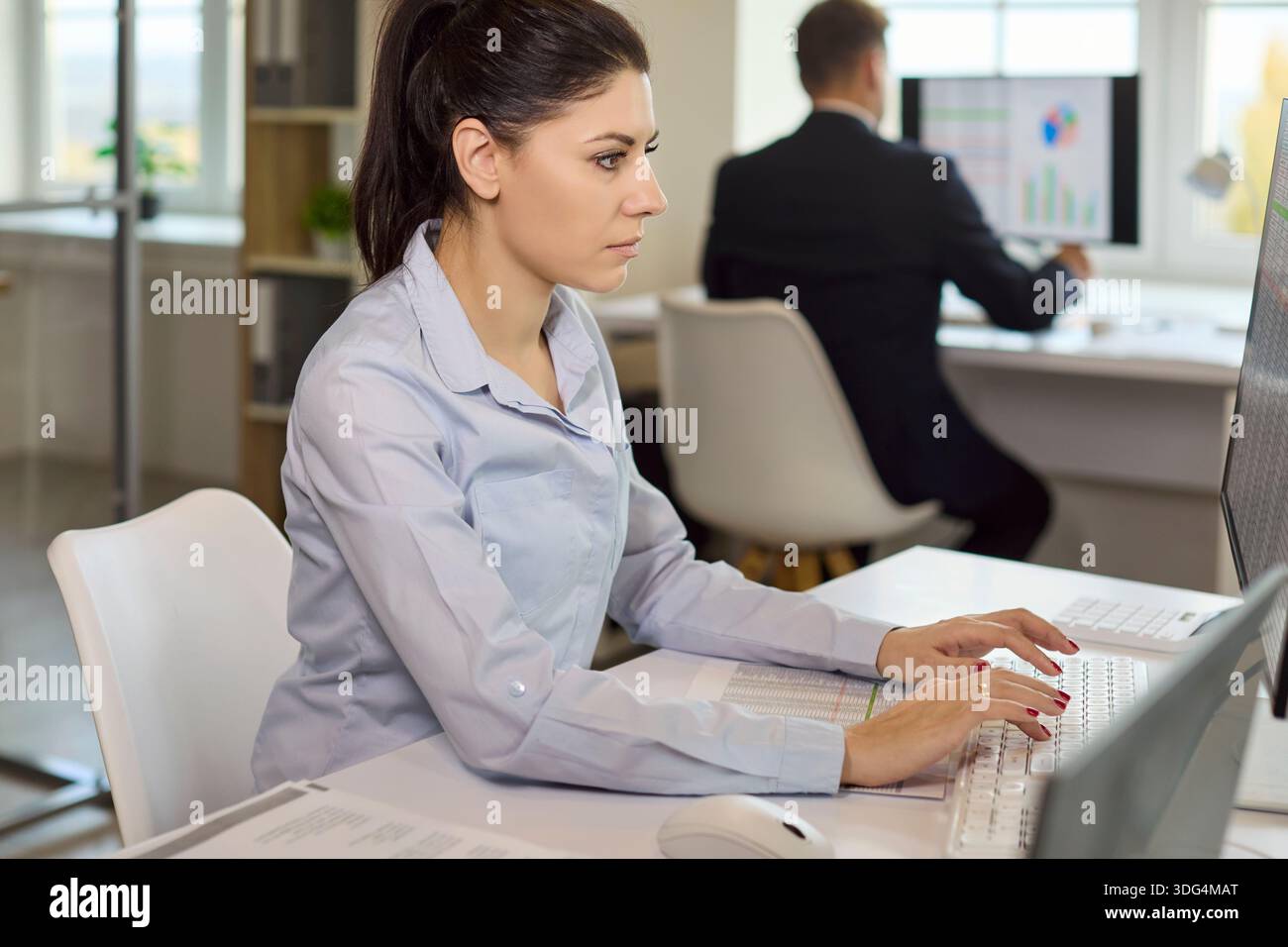 Focused office analyst typing financial data on computer while colleague works Stock Photo