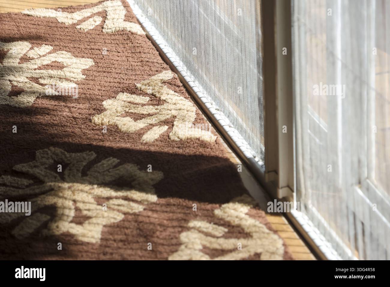 Brown patterned rug next to white sliding glass door frame with screen mesh showing sunny light shadow creates calm peaceful atmosphere in home interi Stock Photo