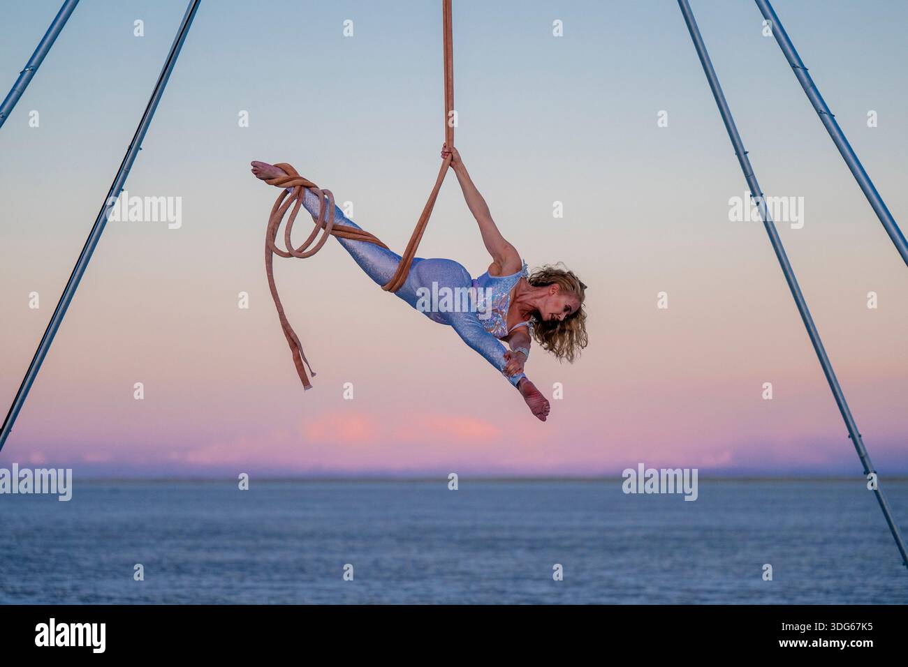 Aerial performer in silver outfit skillfully hangs on ropes over the ...