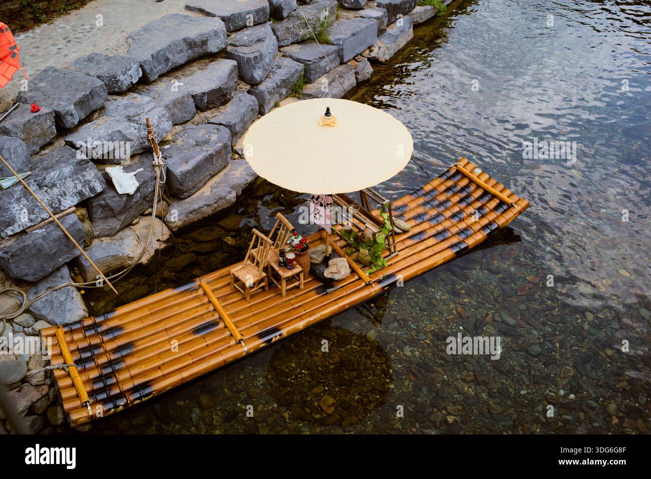 Bamboo raft with an umbrella and chairs floating near stone steps on a ...