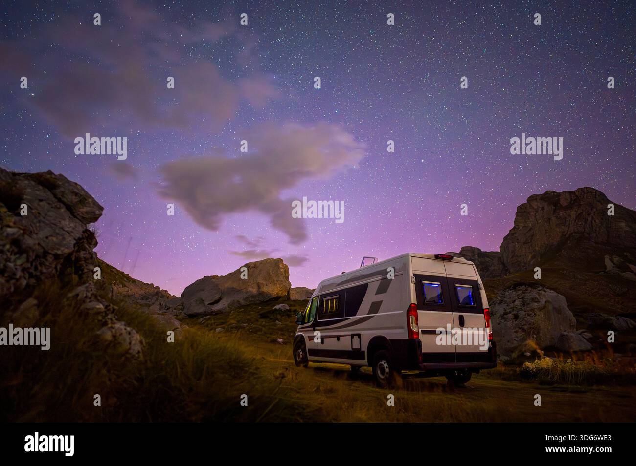 A camper van parked under a vibrant starry night sky at Sedlo Pass in ...