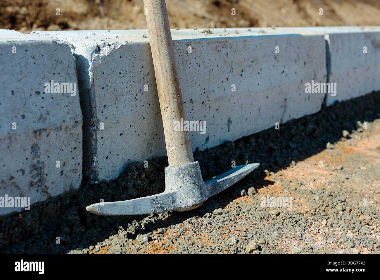 Pickaxe Leaning Against Concrete Curb at Construction Site Stock Photo