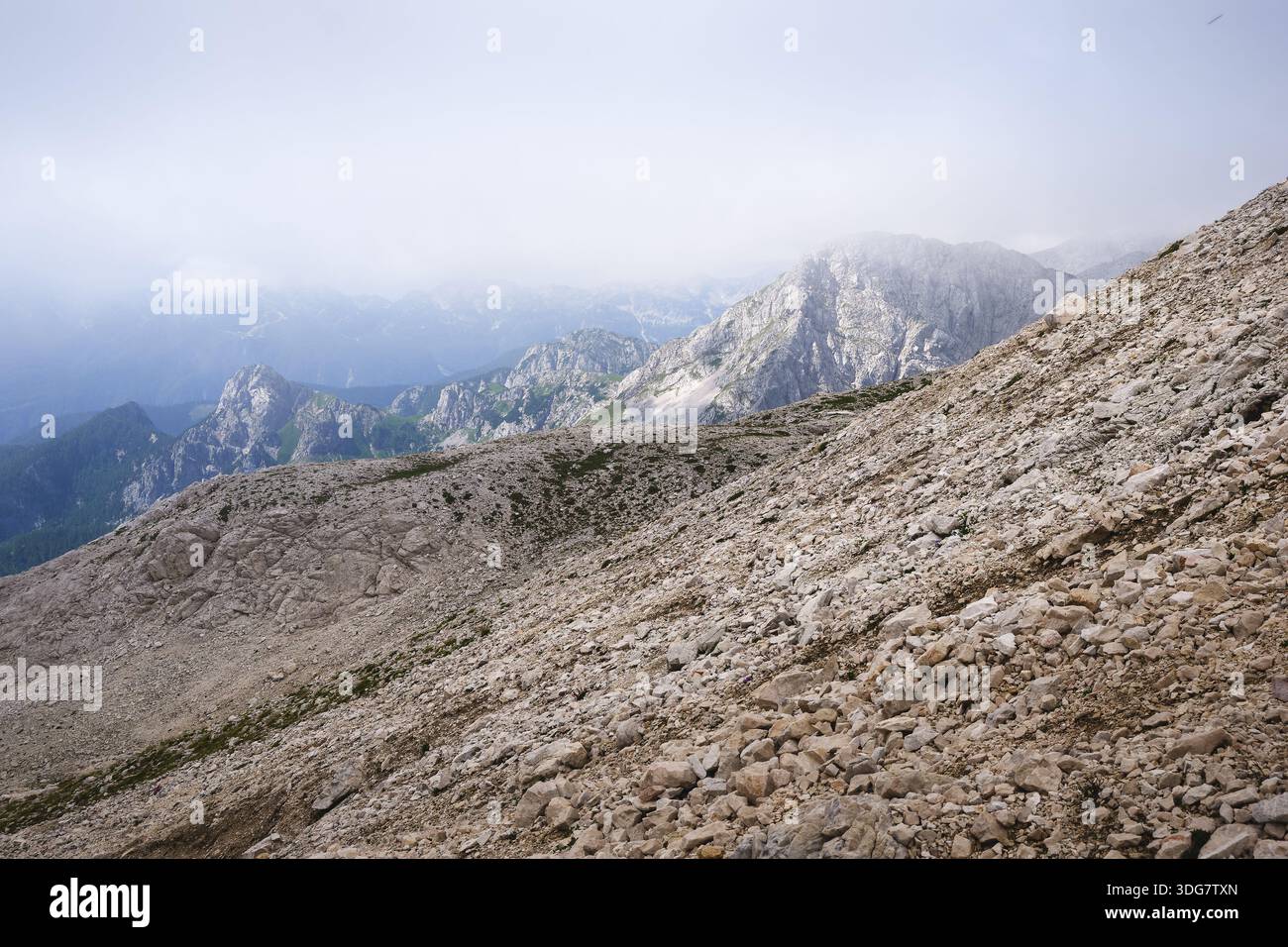 Stunning, misty view of Triglav mountain range with sharp mountain ridges under a cloudy sky Stock Photo