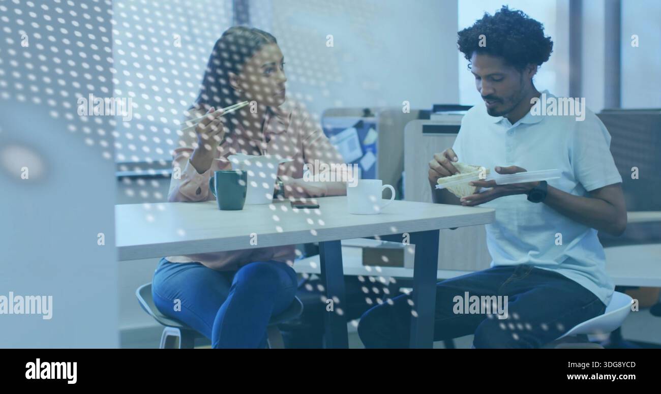 Eating two coworkers in business clothes, sitting in office kitchen with takeout and dotted glass Stock Photo