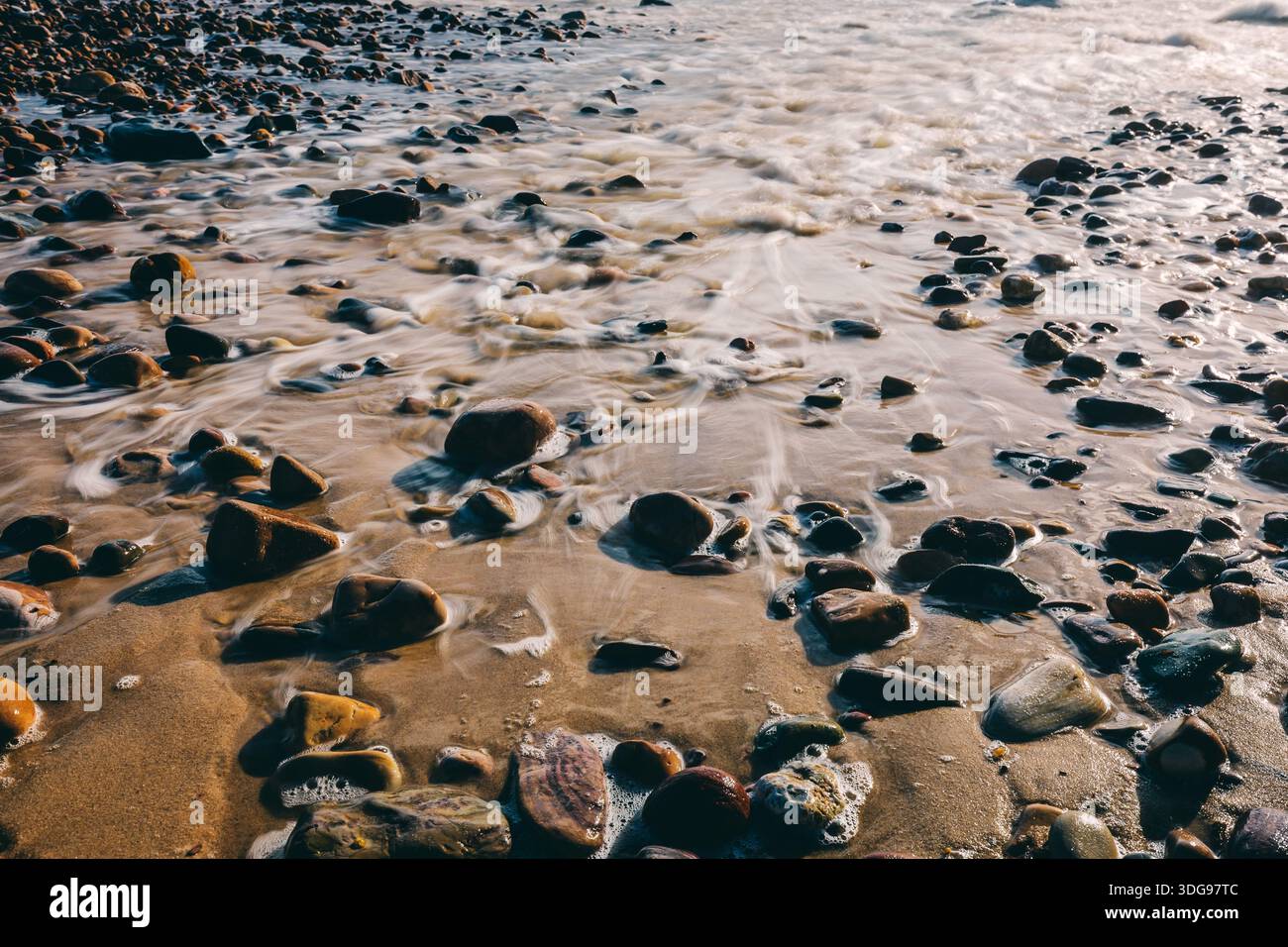 Water flowing over rocks and pebbles on a beach, capturing motion and ...