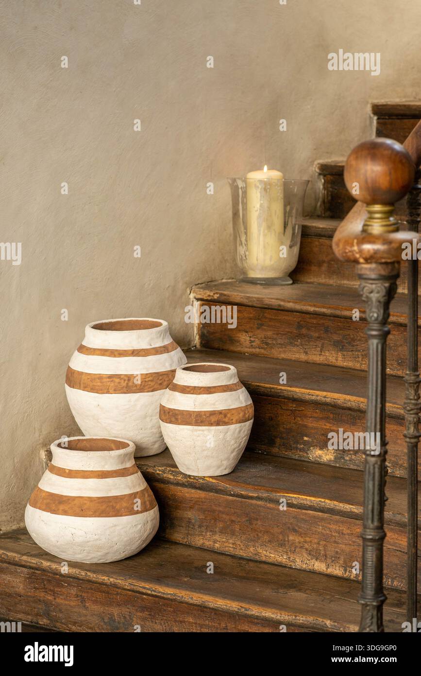 Three handcrafted clay vases with white horizontal stripes arranged on a wooden ledge in a rustic interior setting. Stock Photo