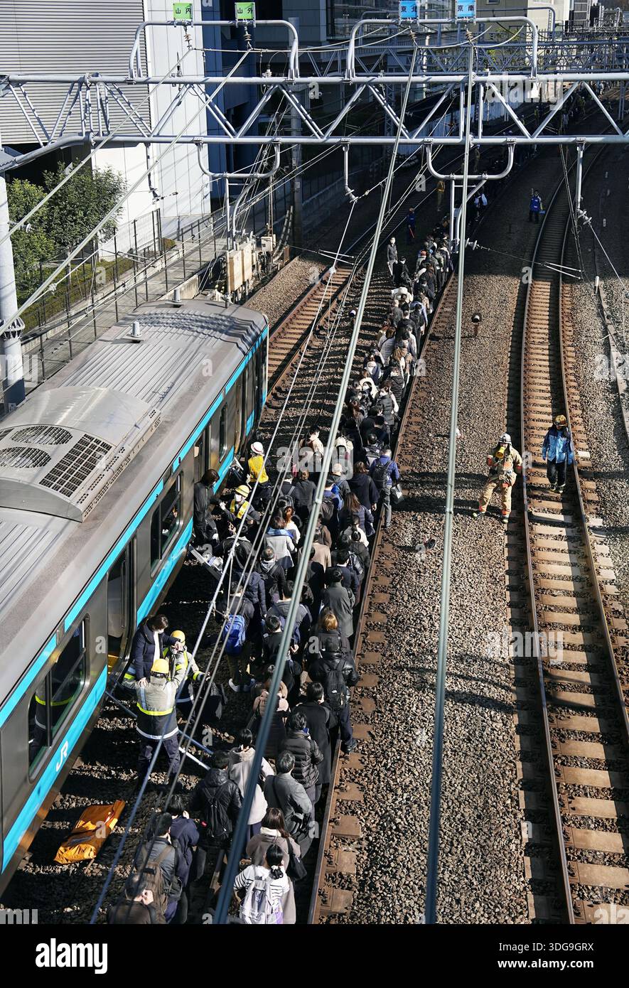 Passengers walk along a track after a power outage halted their train ...