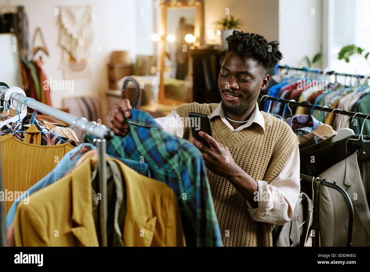 Young Adult Black Man Checking Second Hand Clothing While Using Smartphone Stock Photo
