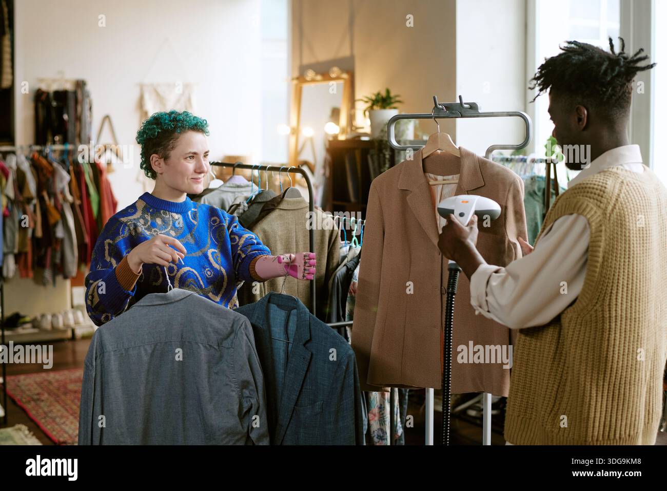 Young Caucasian Woman and Black Man Sorting Second Hand Clothing in Store Stock Photo
