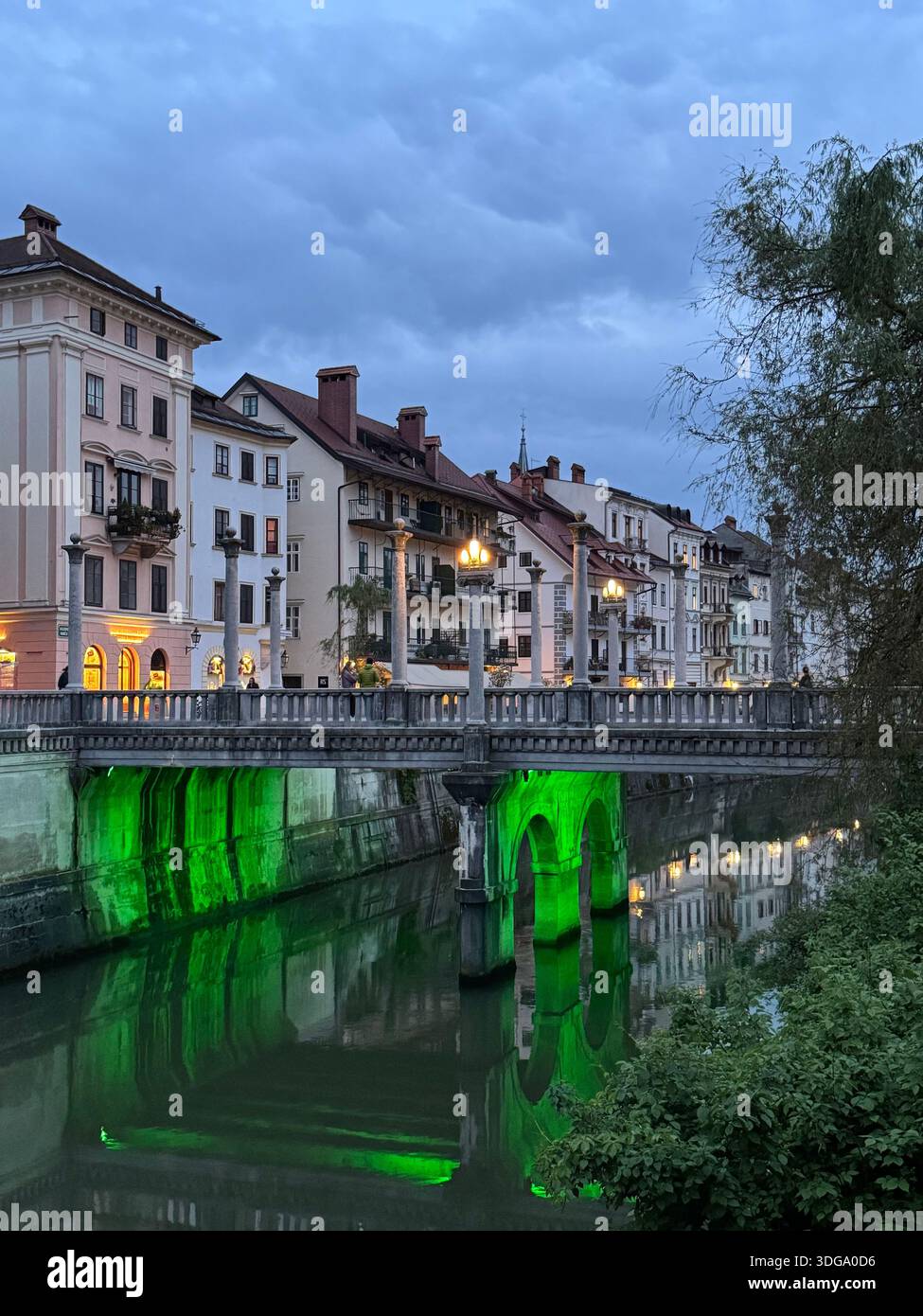 Twilight view of Ljubljana’s iconic Tromostovje, glowing with green lights above the tranquil river - Smartphone Captured Stock Image