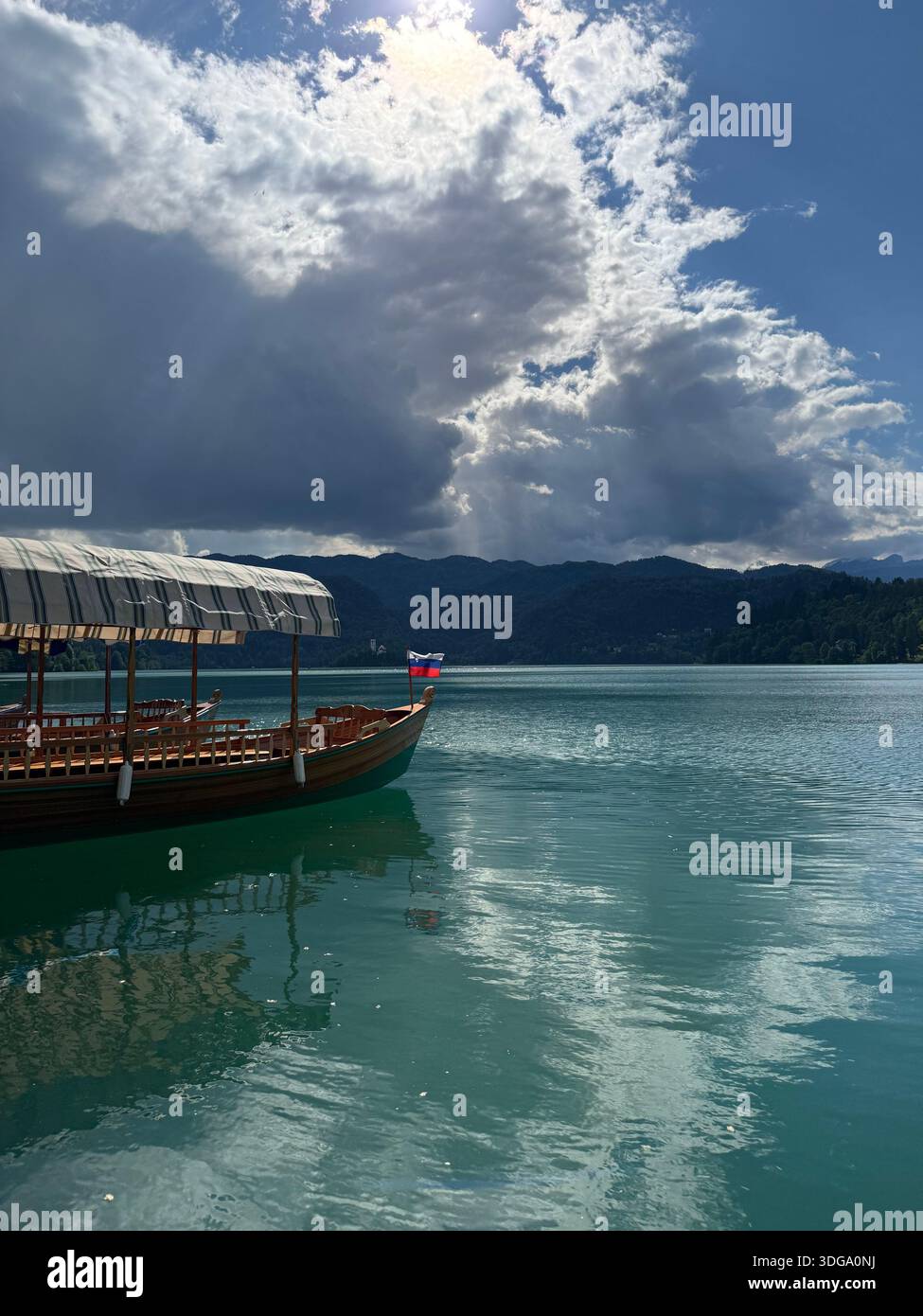 A traditional pletna with striped canopy floats on turquoise waters beneath dramatic clouds in Bled, Slovenia - Smartphone Captured Stock Image