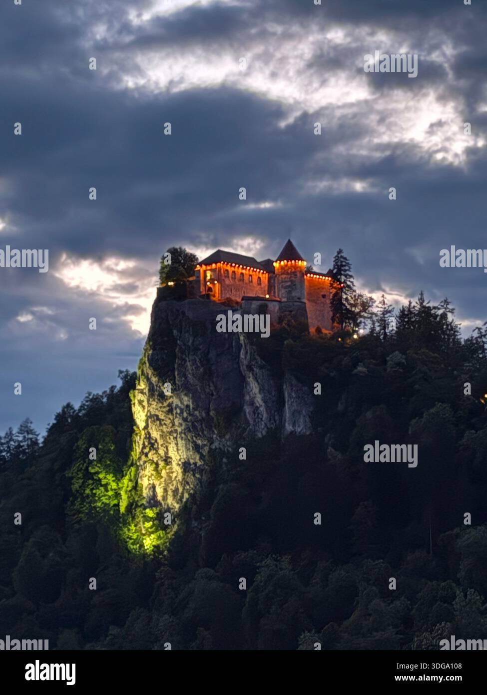Illuminated castle on forested cliff under dramatic evening sky — scenic alpine architecture and landscape - Smartphone Captured Stock Image