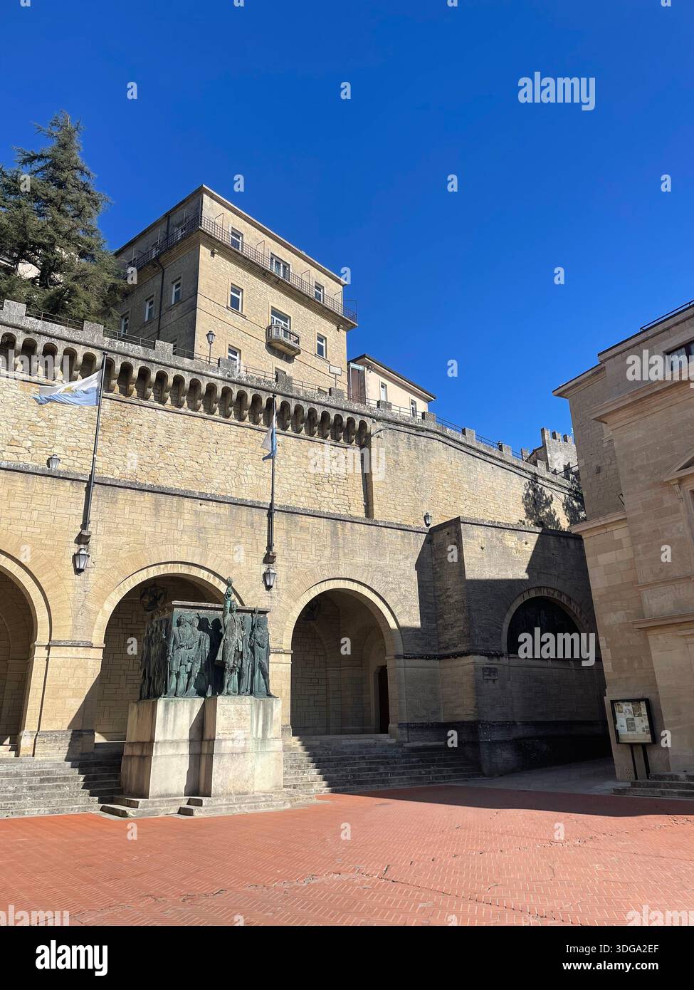 Historic civic square and stone architecture in San Marino, featuring arches and a public monument beneath clear blue skies in the old town. - Smartphone Captured Stock Image