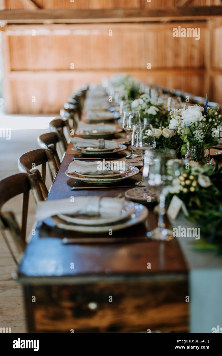 rustic table set for dinner with flower arrangements in a barn Stock Photo