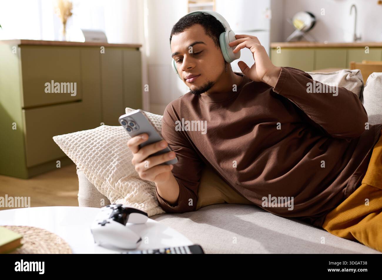 Handsome young man relaxes on the sofa, listening to music while using his phone. Stock Photo