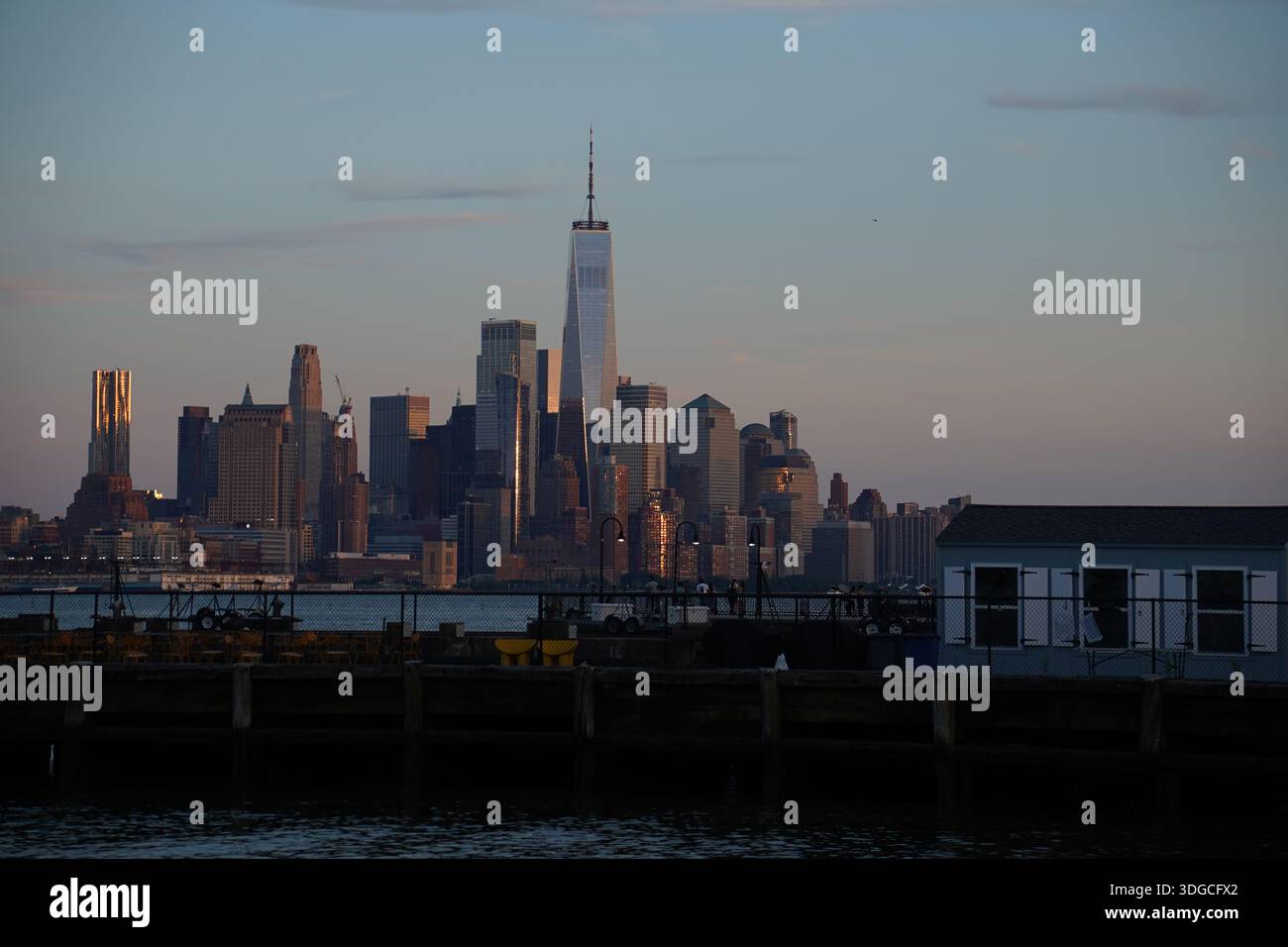 New York. It’s skyline of Manhattan at dusk, viewed from Hoboken Pier, New Jersey with illuminated skyscrapers and waterfront reflections. Stock Photo