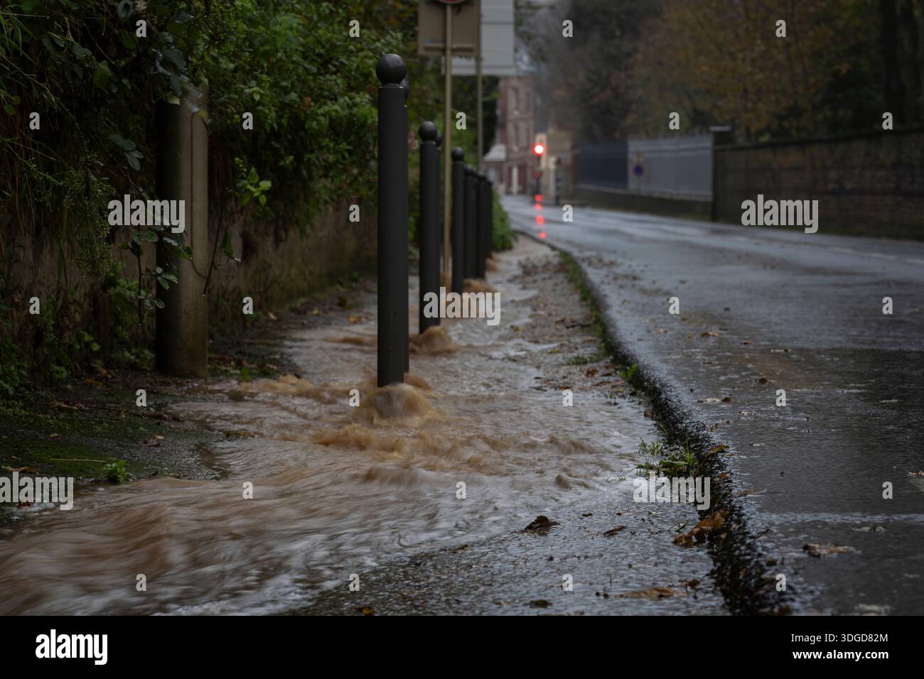 Floodwater rushing along a city street after heavy rainfall, overflowing the sidewalk and drainage system in an urban area. Urban flooding. Stock Photo