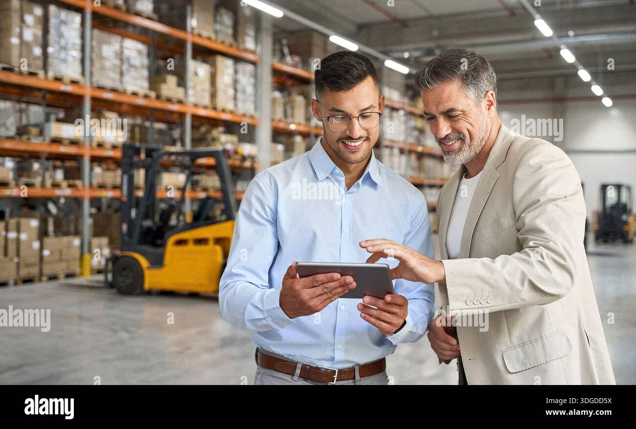 Warehouse managers team standing near cardboard boxes using tablet. Stock Photo
