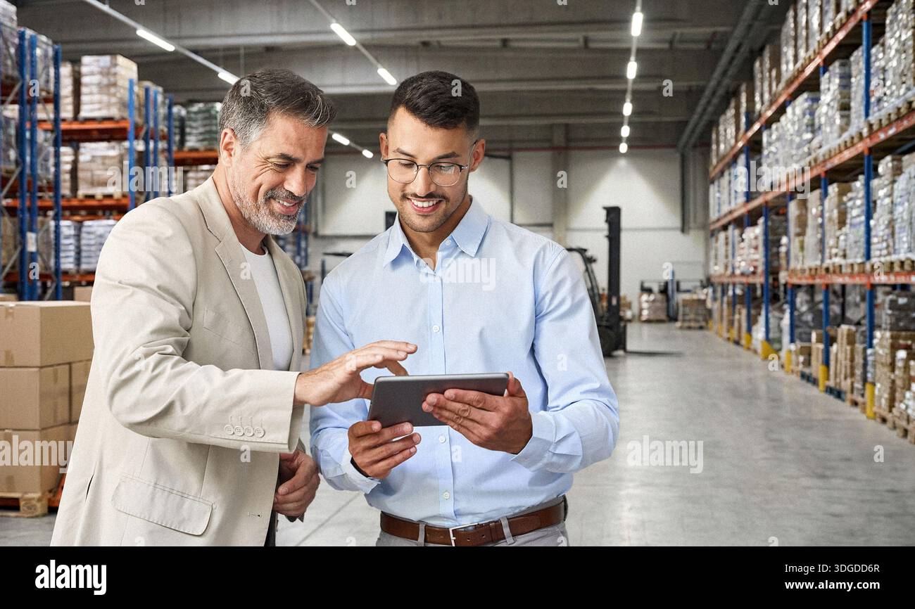 Warehouse managers team standing near cardboard boxes using tablet. Stock Photo