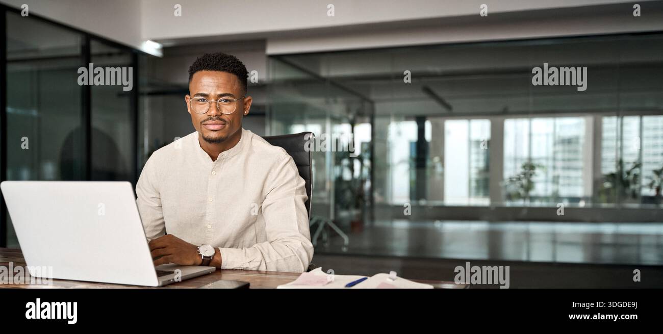 Confident professional African business man looking at camera using computer. Stock Photo
