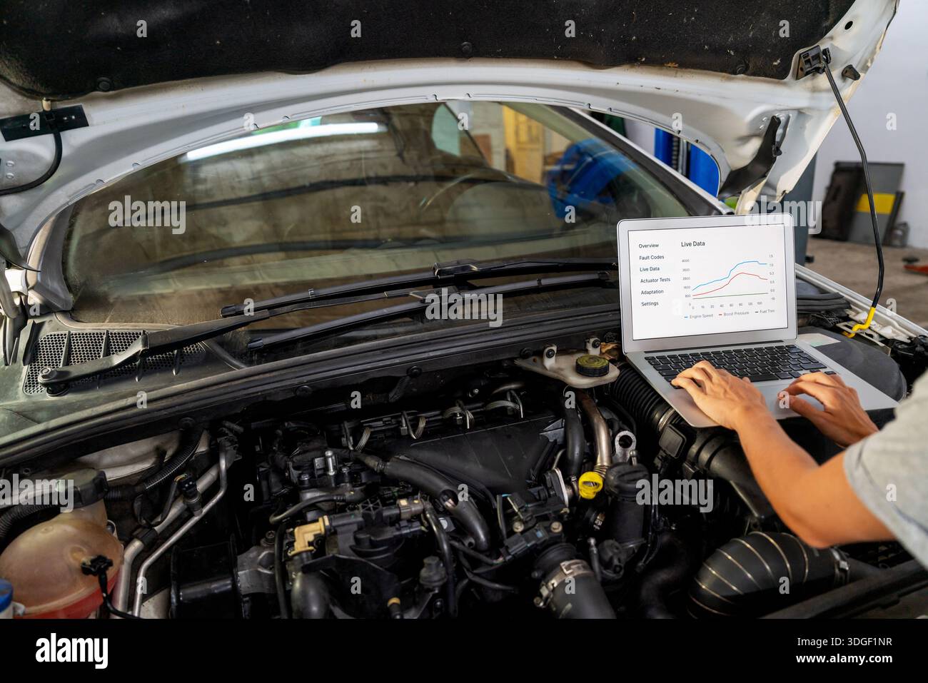 Auto mechanic performing car diagnostics using laptop under open hood Stock Photo