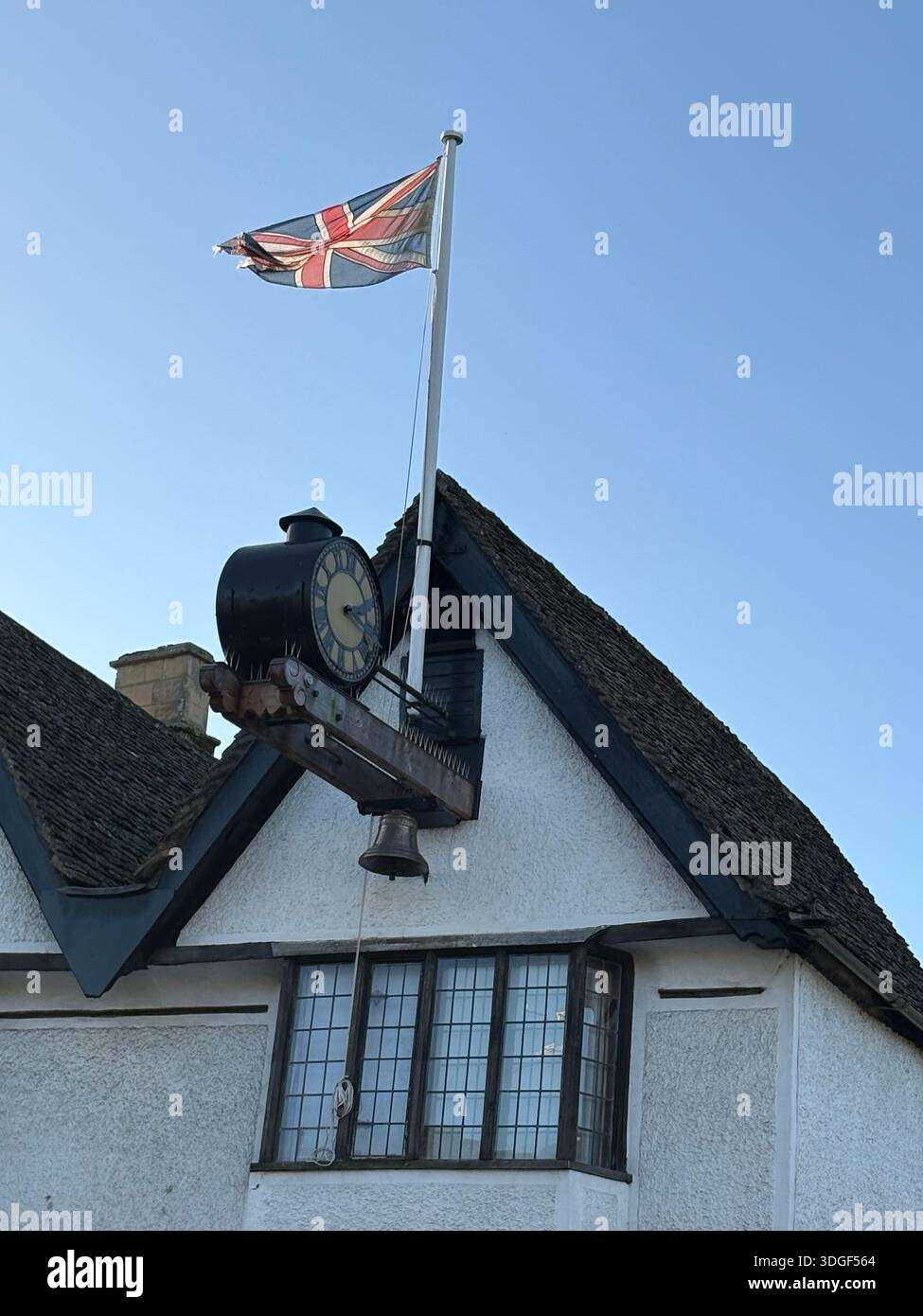 Union Jack flag flying above a traditional British building with a historic clock sign against a clear blue sky in England. - Smartphone Captured Stock Image