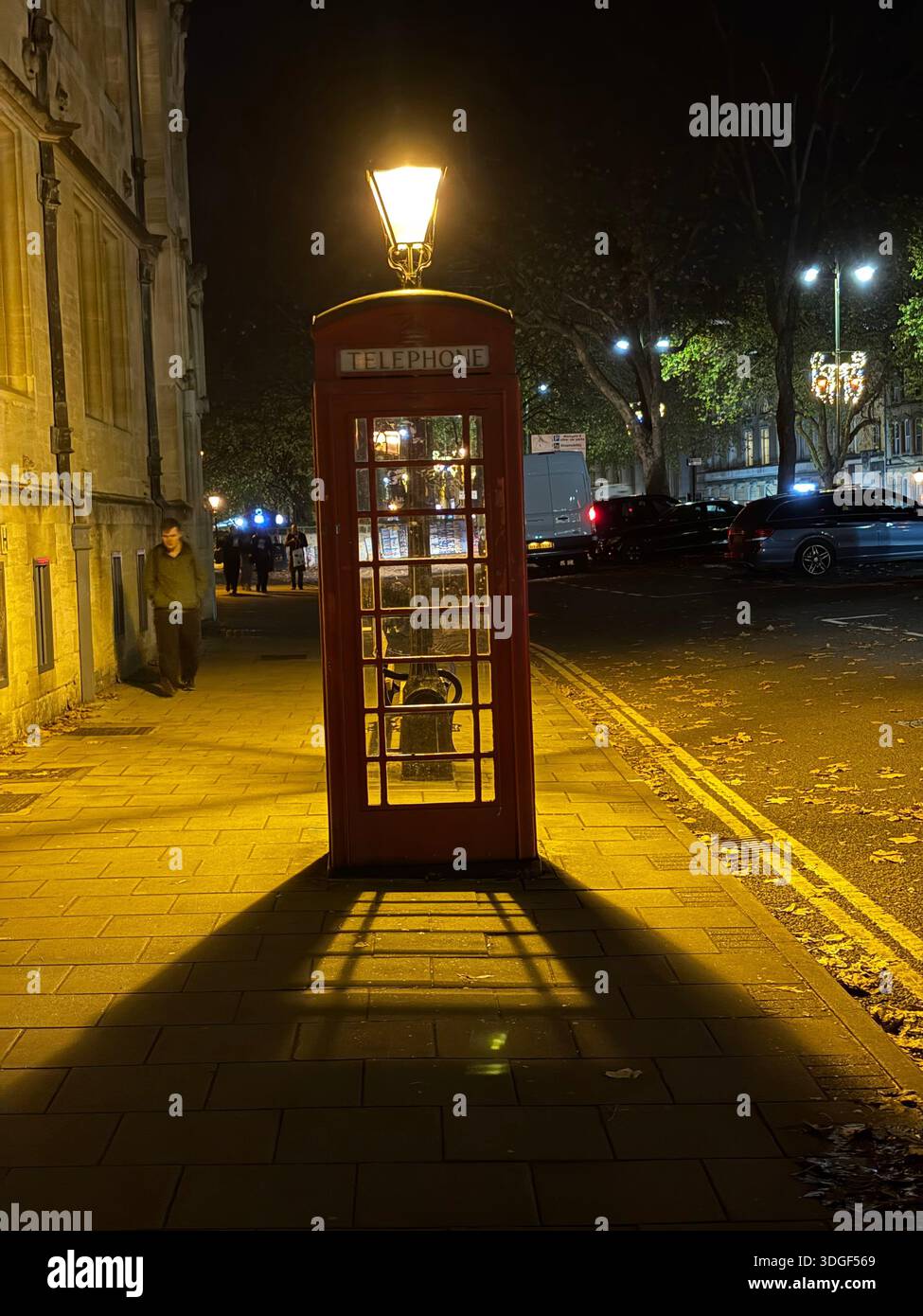Classic red British telephone box illuminated at night on a quiet city street, creating a nostalgic urban scene in England - Smartphone Captured Stock Image