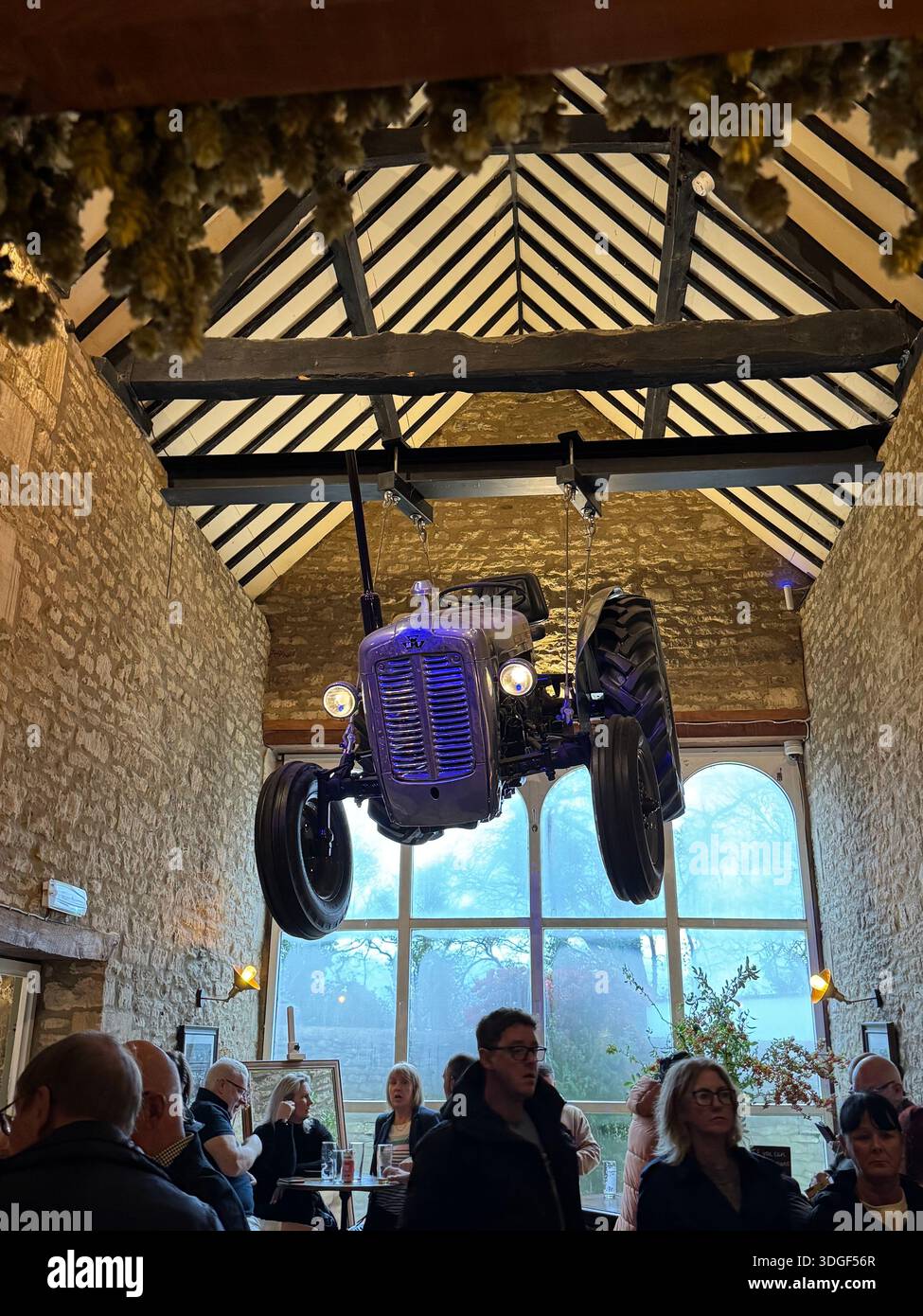Visitors gathered inside the Farmer's Dog with a vintage tractor suspended from wooden beams, creating a unique countryside interior scene. - Smartphone Captured Stock Image