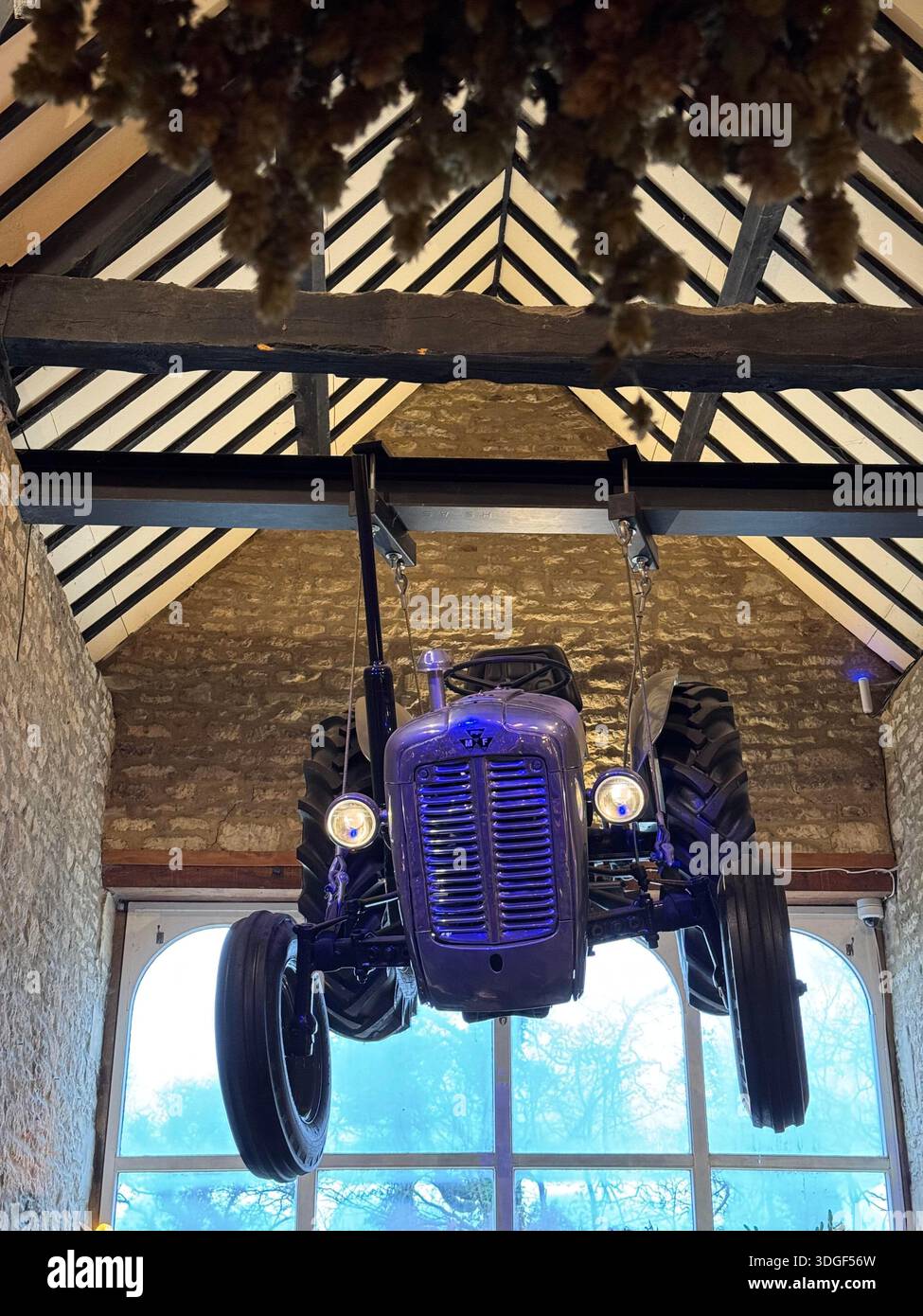 Visitors gathered inside the Farmer's Dog with a vintage tractor suspended from wooden beams, creating a unique countryside interior scene. - Smartphone Captured Stock Image