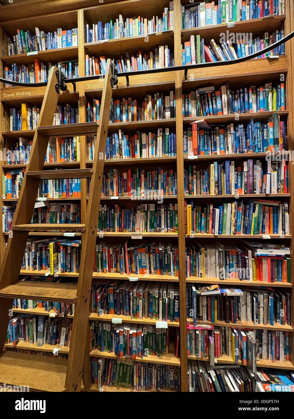 Tall bookshelves filled with colourful books and a wooden ladder inside an independent bookstore, creating a cosy literary interior. - Smartphone Captured Stock Image
