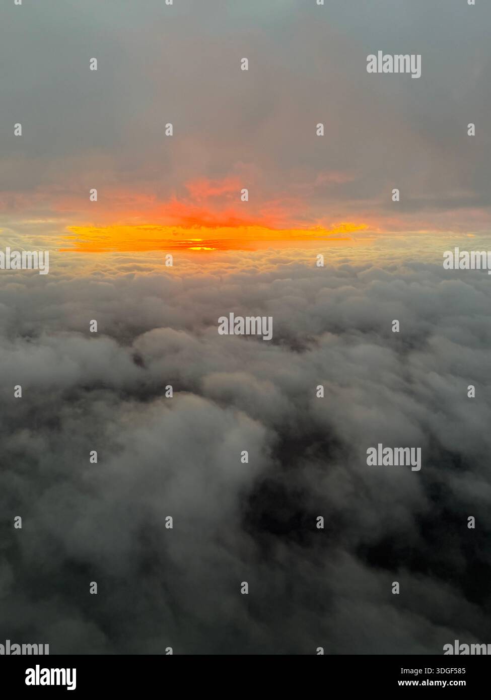 Aerial view above thick cloud layer with glowing orange sunset breaking through the horizon, creating a dramatic and atmospheric sky scene - Smartphone Captured Stock Image