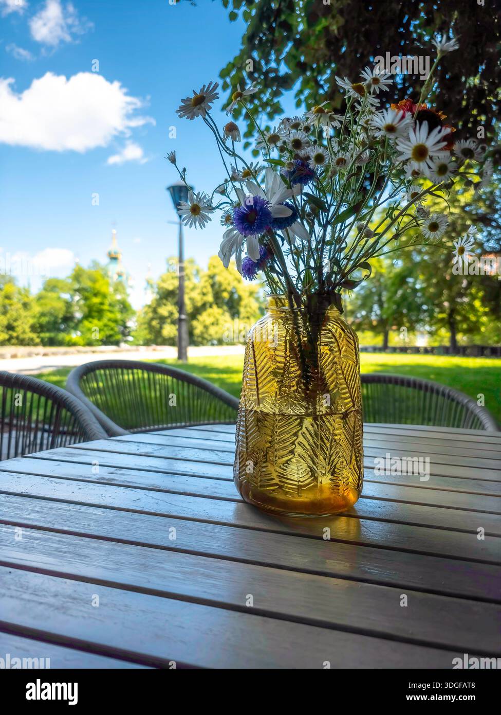 A textured yellow vase with daisies and cornflowers on a wooden table in a cafe in Kyiv's historic center, near the foundation of the Desyatynna Churc - Smartphone Captured Stock Image