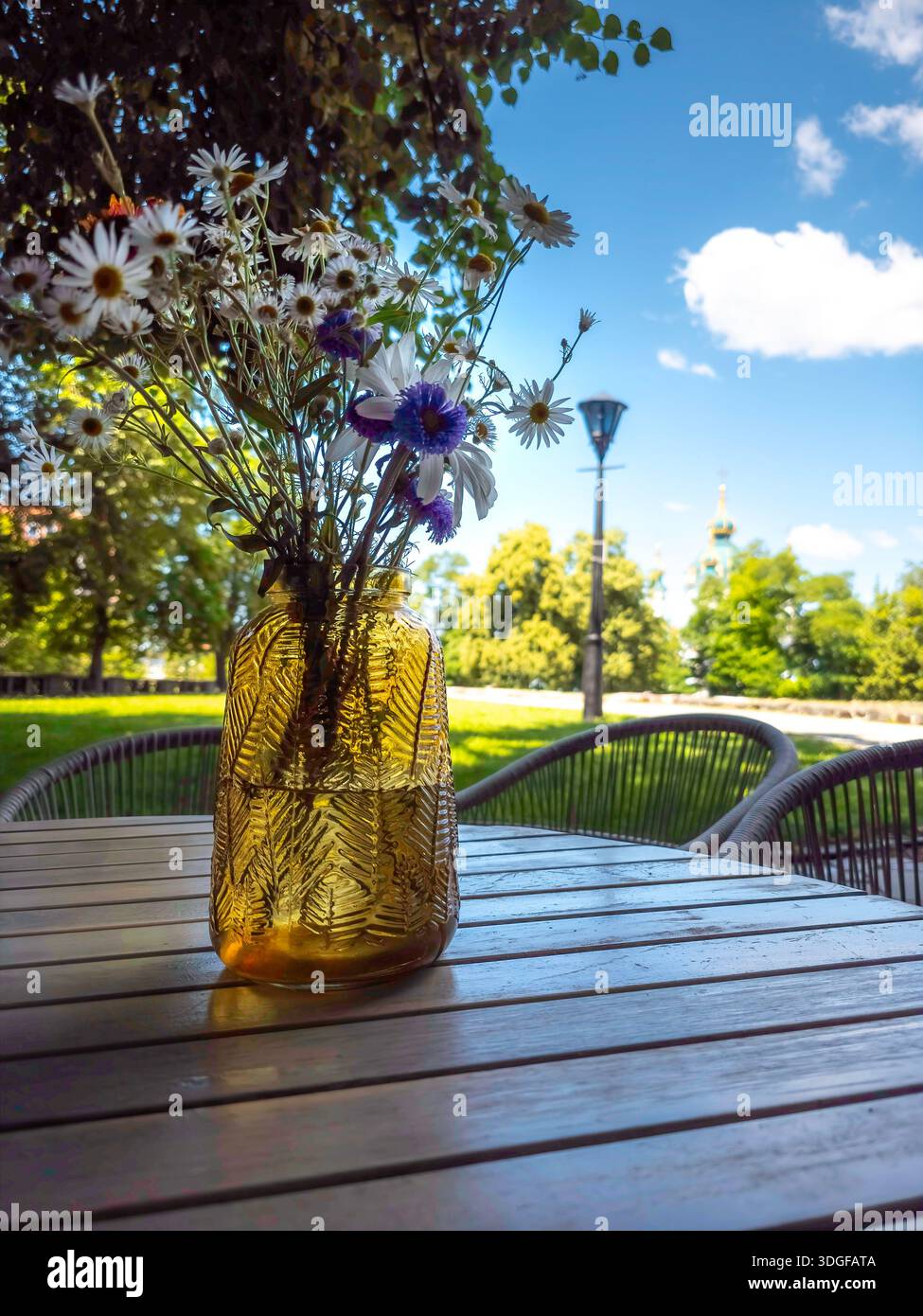 A textured yellow vase with daisies and cornflowers on a wooden table in a cafe in Kyiv's historic center, near the foundation of the Desyatynna Churc - Smartphone Captured Stock Image