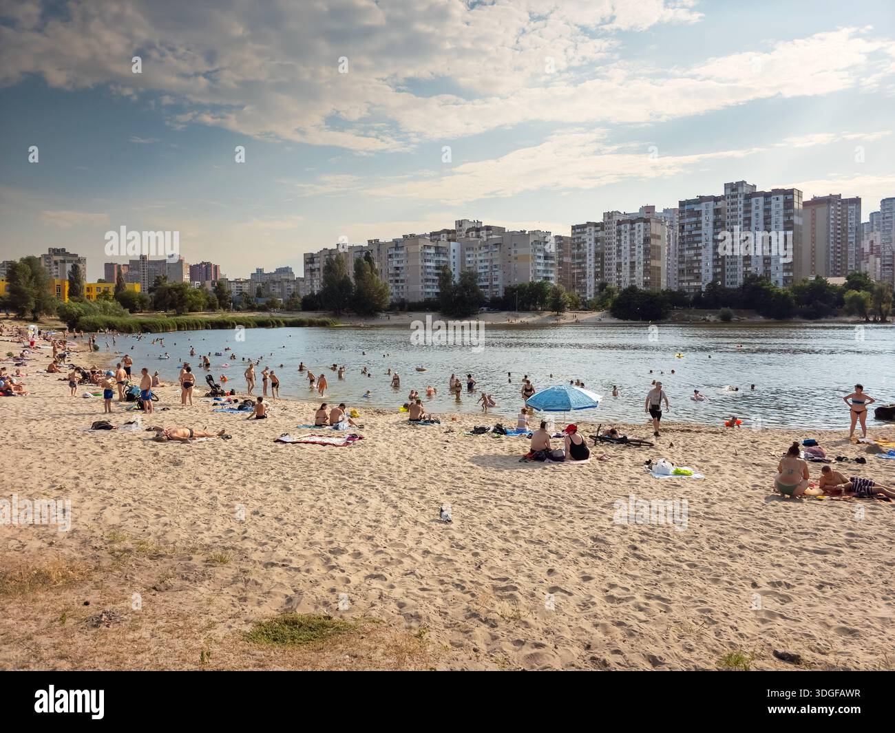 Kyiv, Ukraine - July 14, 2025: A sandy beach on Sonyachne Lake with people relaxing and swimming at hot july afternoon. A high rise residential buildi - Smartphone Captured Stock Image