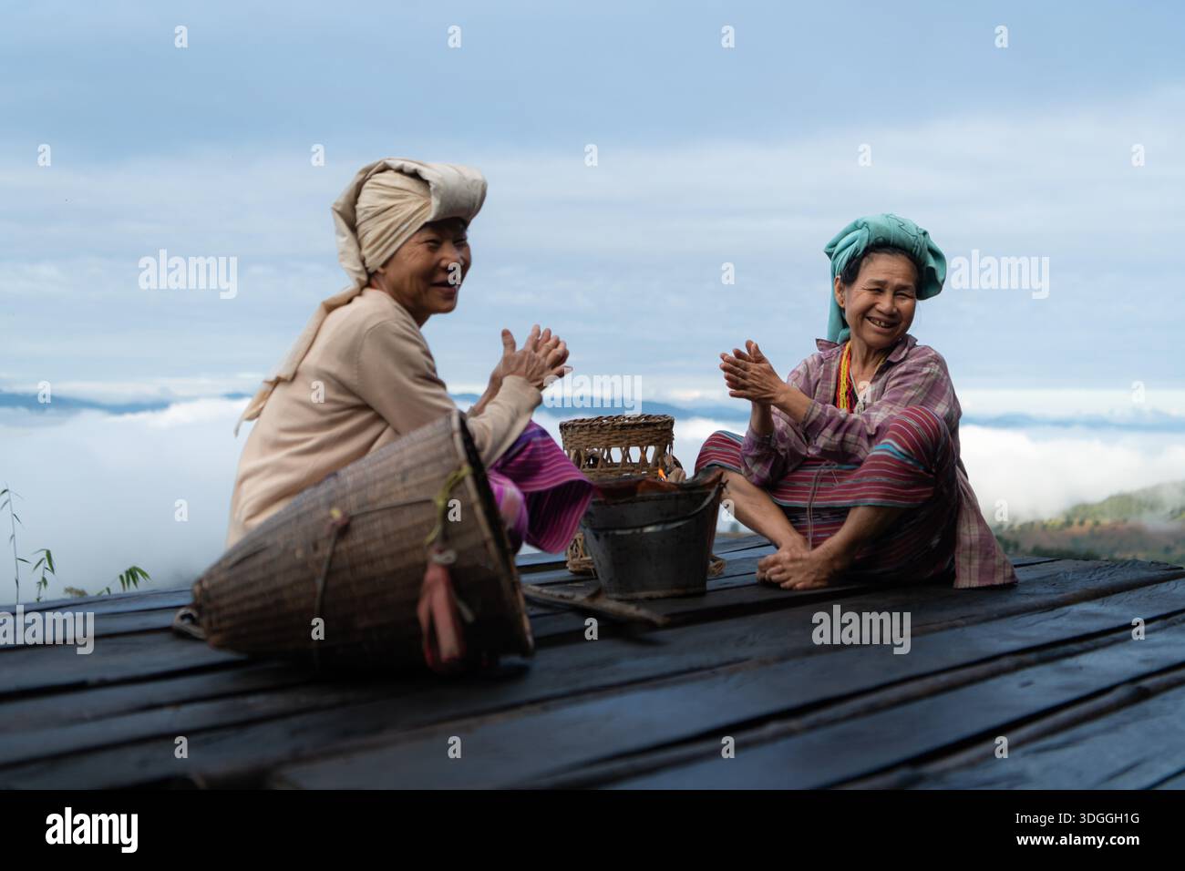 Two Asian rural women sitting together on a wooden platform, sharing ...