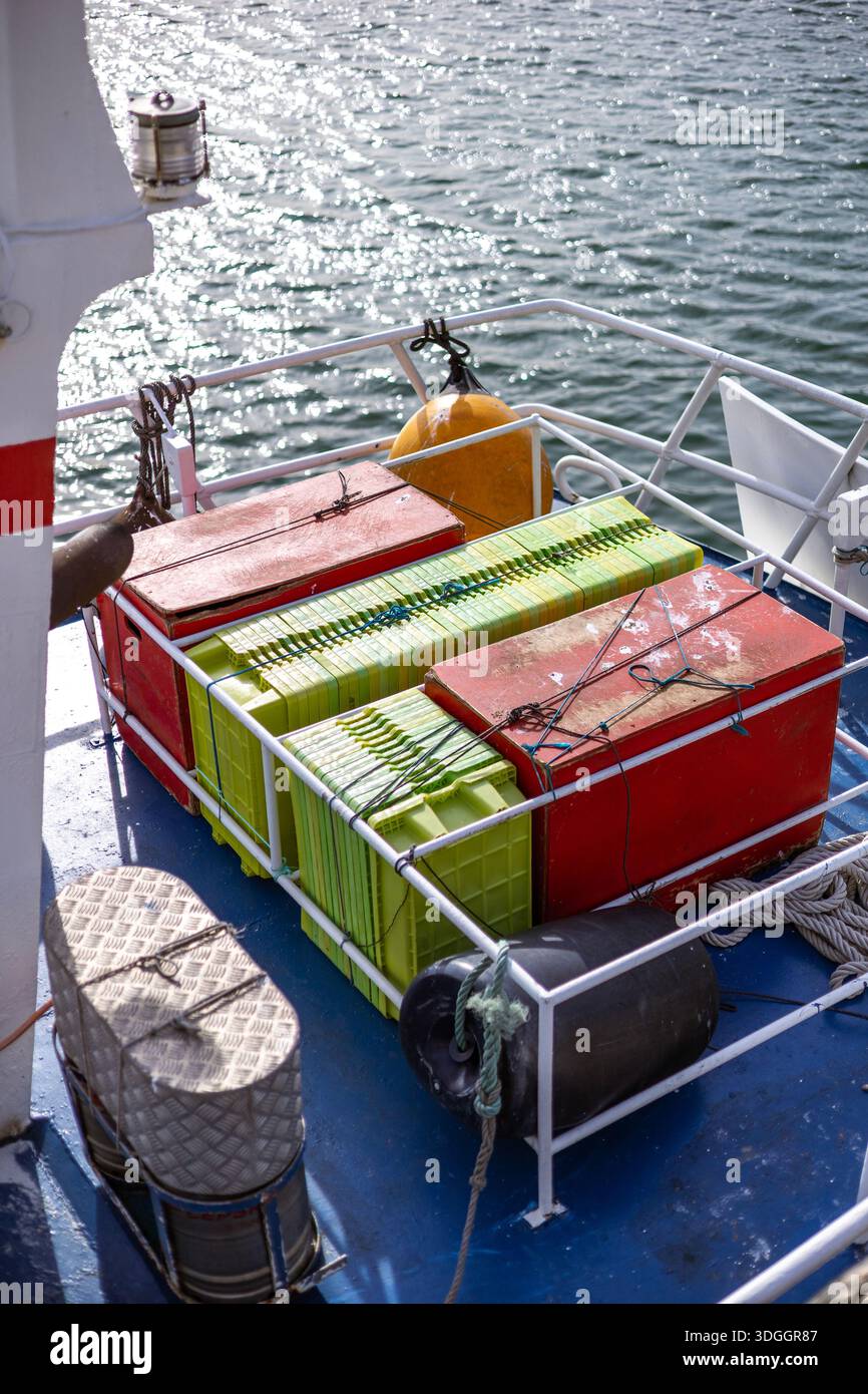Colorful plastic fish crates are stacked on the blue deck of a boat ...