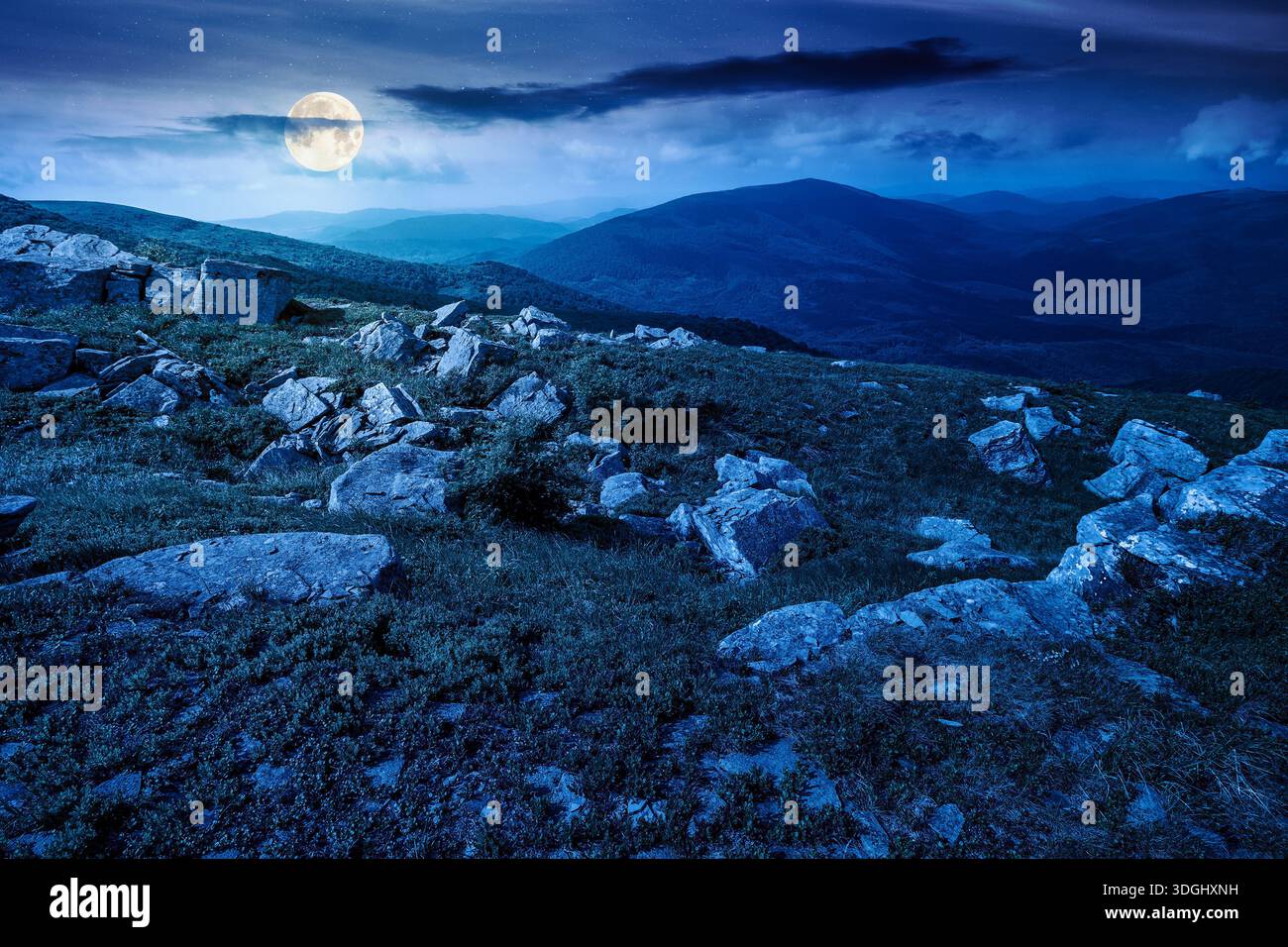mountain landscape in summer with rocks at night. grass under dark sky in full moon light. alpine meadow and rolling hills with boulders. backdrop for Stock Photo
