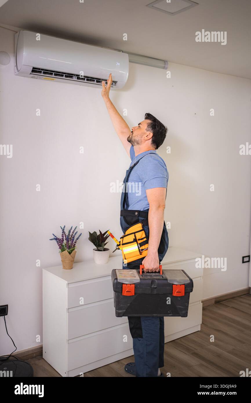 Technician checking air conditioning unit while holding toolbox Stock Photo