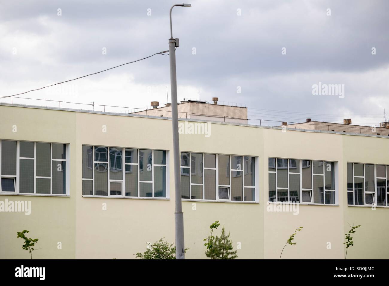 The pale yellow exterior of a school gymnasium. Long horizontal windows, fitted with protective netting on the inside, indicate a space for indoor spo Stock Photo