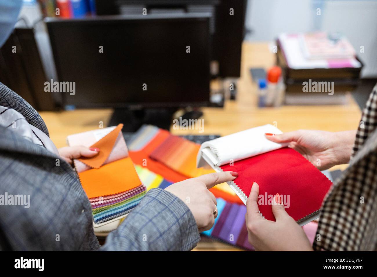 Two designers or a client and a decorator collaborating on a project. They are choosing from a variety of colorful fabric swatches for fashion or inte Stock Photo