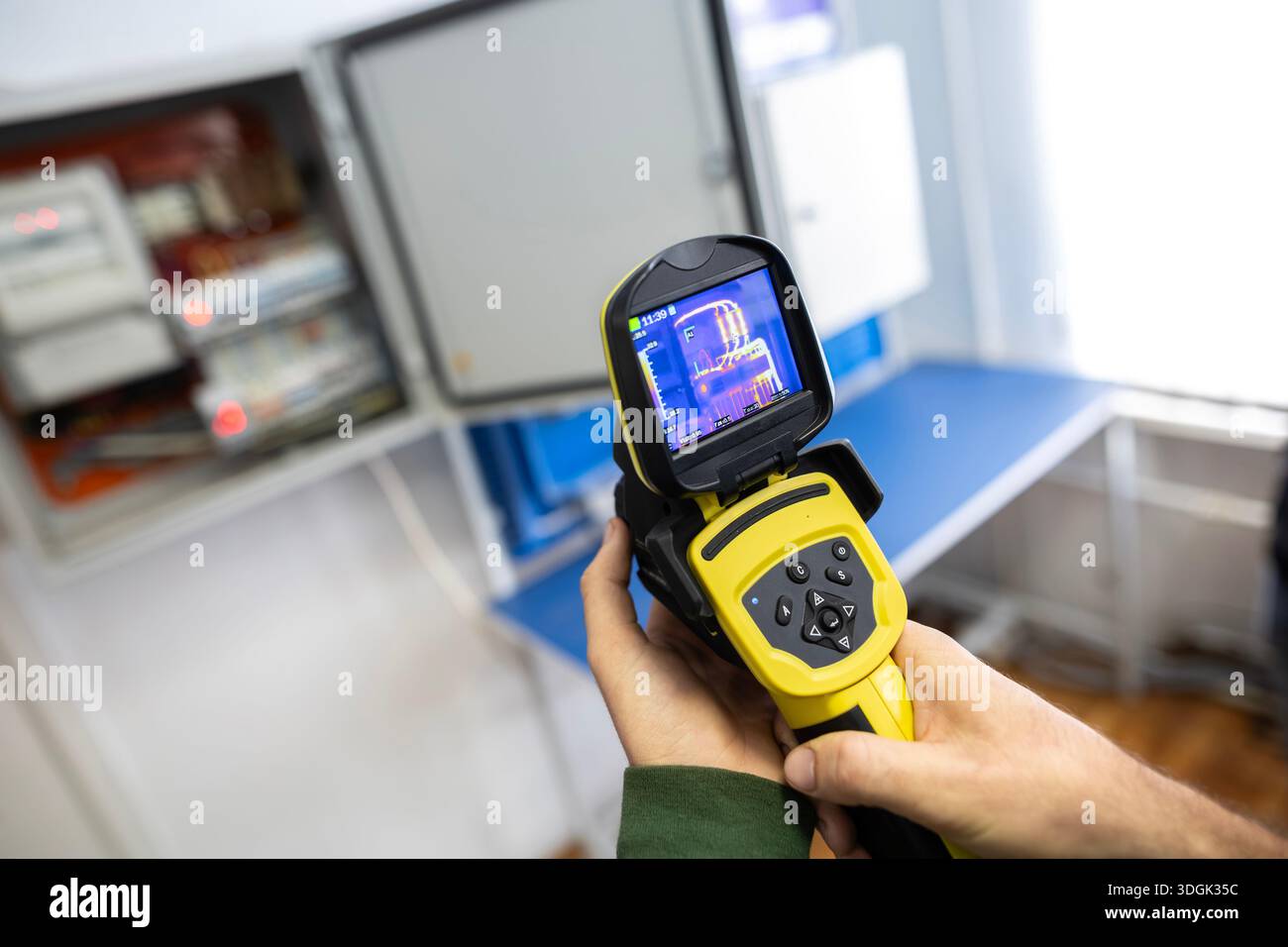 An electrician's hand holds a thermal imaging camera to inspect an open electrical panel, checking for overheating components, hotspots, and potential Stock Photo