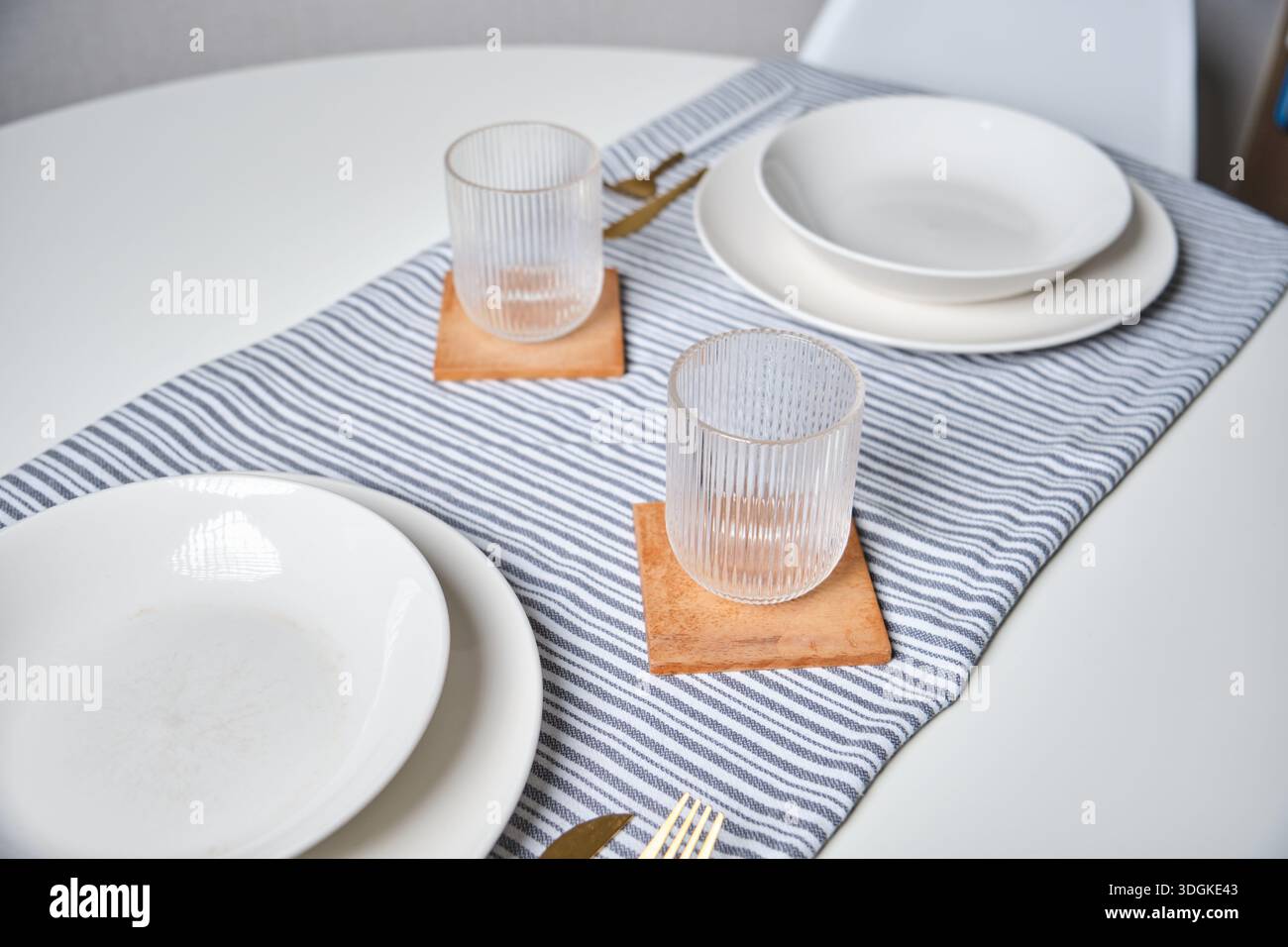 Dining table set for two with plates, glasses, and a striped table runner Stock Photo