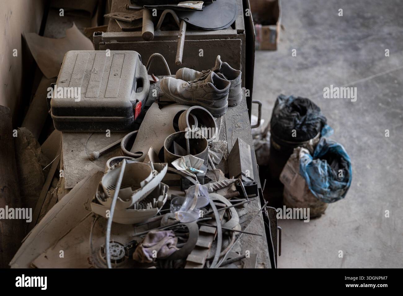 A cluttered workbench holds a black toolbox, worn work boots, tangled ...